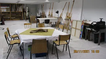 Ein Atelier mit Tischen, Stühlen und Malutensilien.