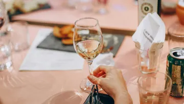 Wine glass is held surrounded by tables and glasses.