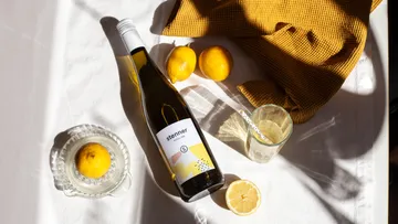 Wine bottle is lying on table with lemons and glass.