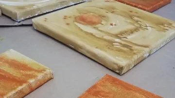 Canvases with colorful paintings lie on a table.
