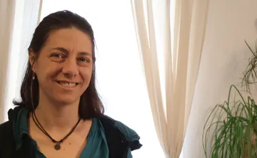 Frau lächelt im Zimmer neben einem Fenster und Pflanzen.
