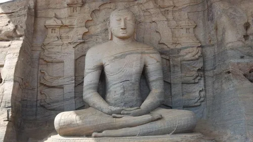 Massive Felsstatue sitzt meditierend in natürlicher Umgebung.