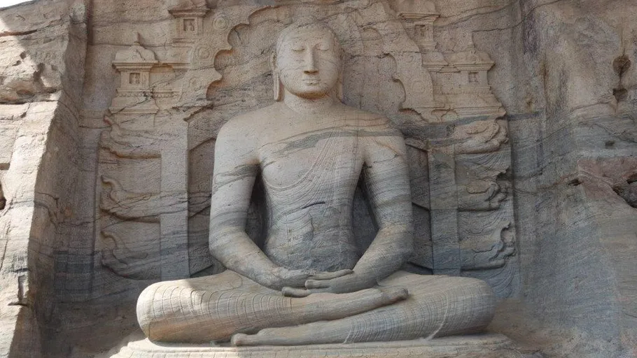 Massive Felsstatue sitzt meditierend in natürlicher Umgebung.
