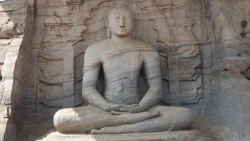 Seated Buddha statue in rock surrounded by reliefs.