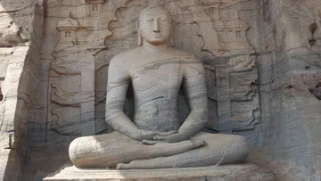 Sitzende Buddha-Statue, umgeben von steinernen Felswänden.