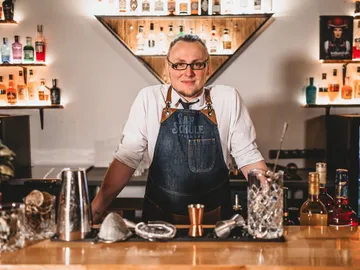 Bartender is standing behind the bar with spirits, smiling.