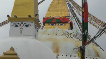 Stupa mit bunten Gebetsfahnen und Tauben, umgeben von Wolken.