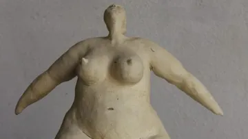 Eine Statue einer fülligen Frau steht mit erhobenen Armen.