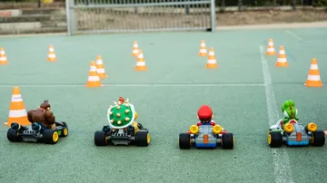 Four small vehicles drive on a green square between pylons.