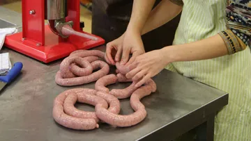 Hands making sausages using a sausage stuffer.
