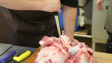 A cook cuts meat on a wooden board.