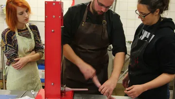 Butcher works on a sausage machine with two spectators.