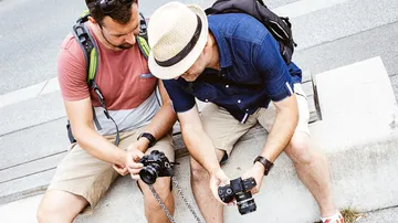Two men review photos on their outdoor cameras.