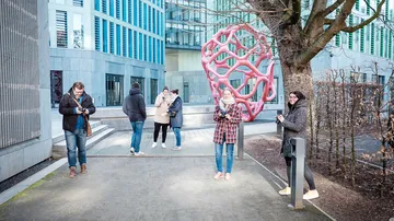 Fünf Menschen stehen um eine rote Skulptur in einer Stadt.