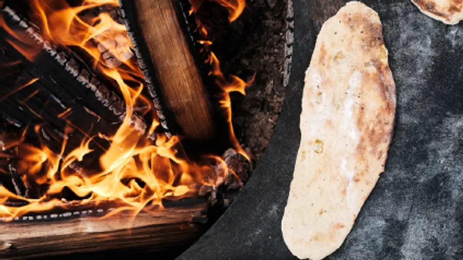Fladenbrot wird über offenen Feuer gebacken, Holz brennt.