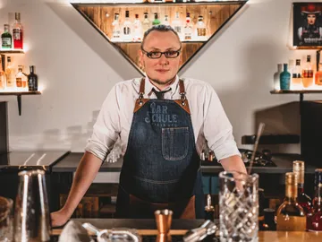 Bartender stands at the counter, surrounded by drinks and glasses.