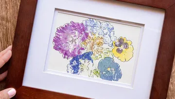 A framed painting with colorful flowers is lying on a table.