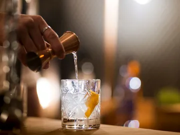 Hand gießt Alkohol in ein Glas mit Eiswürfeln.