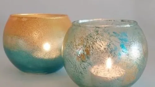 Zwei Teelichthalter leuchten, vor neutralem Hintergrund.