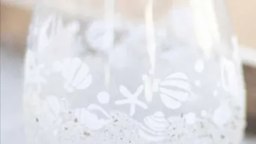 Glas mit maritimen Motiven, gefüllt mit Wasser und Sand.