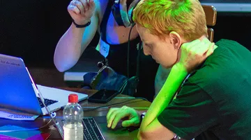 Junger Mann arbeitet konzentriert am Laptop in lebhaftem Licht.
