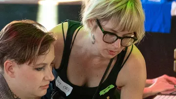 Zwei Frauen arbeiten gemeinsam an einem Tisch in einem Raum.