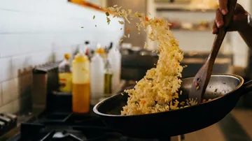 Pfanne mit Reis wird mit einem Kochlöffel geworfen.