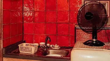 Sink with dishes, fan in a red kitchen.