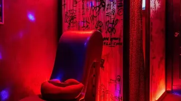 Rote beleuchtete Umgebung, ein Stuhl steht an der Wand.