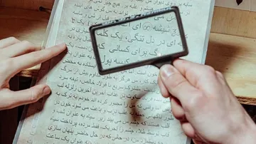 Eine Hand hält eine Lupe über einen Text.