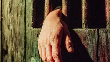Eine Hand greift durch Gefängnisstäbe in einem dunklen Raum.