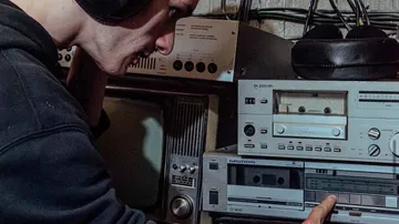 Man operates an old cassette player in a room.