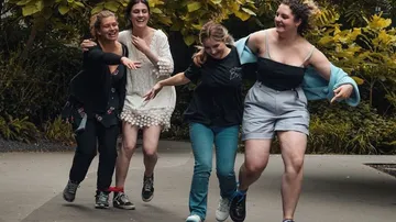 Vier Frauen laufen fröhlich auf einem Weg in einem Garten.