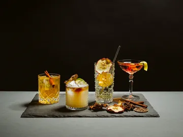 Four cocktails are sitting on a table against a black background.