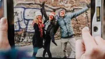 Drei Personen posieren fröhlich vor einer graffitibedeckten Wand.