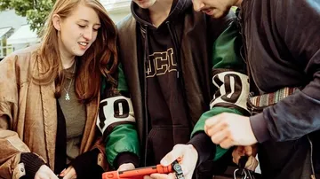Vier Personen betrachten gemeinsam ein Smartphone im Freien.