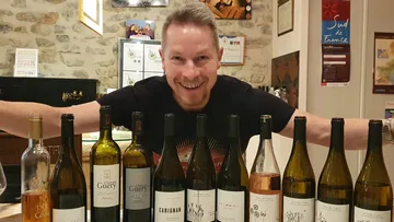 Man smiles with bottles of wine in a restaurant.