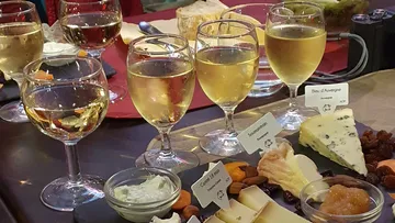 Wine glasses stand next to various types of cheese and snacks.