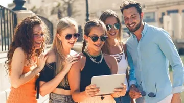 Fünf Personen betrachten gemeinsam ein Tablet in der Stadt.