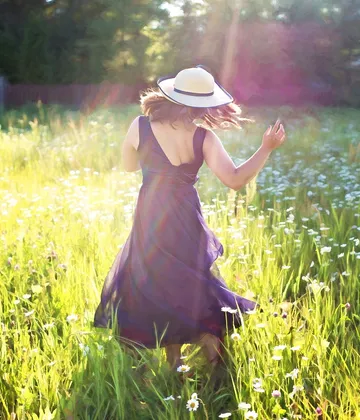 A woman dances happily in a blooming field.