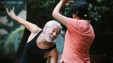 Elderly man joyfully dances with woman in the park.