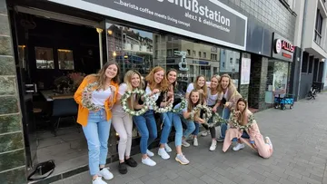 Group of women holding floral wreaths outside cafe.