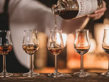 A glass is filled with whiskey from a bottle.