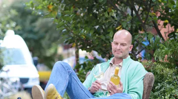 Man sitting with drinks outdoors, surrounded by plants.