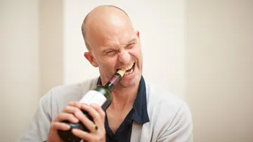 Man bites into a wine bottle to open it.
