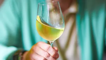 Ein Glas Wein wird mit einer Hand gehalten.