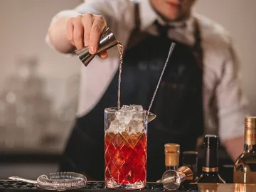 Bartender pours drink into a glass filled with ice.