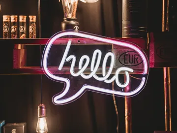 Neonlicht mit dem Wort „hello“ vor dunklem Hintergrund.