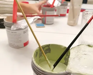 Farbenbehälter mit Pinseln steht auf einem Tisch.