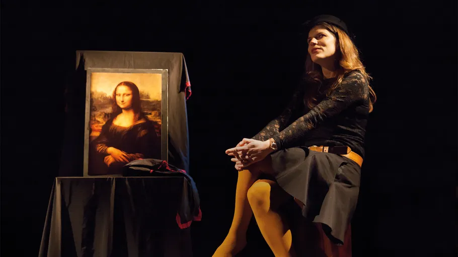 Frau sitzt neben Mona-Lisa-Gemälde auf einer Bühne.